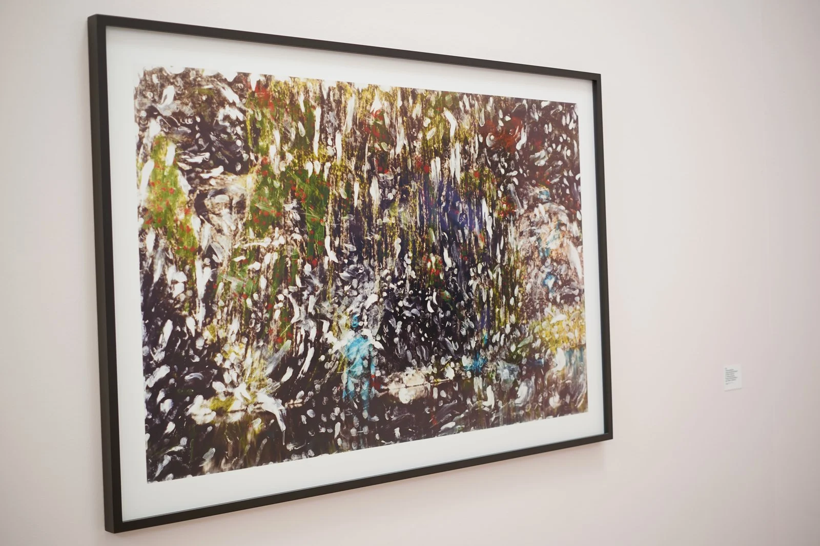 En abstrakt målning i brunt, gult och vitt hänger på vit vägg inuti ett galleri