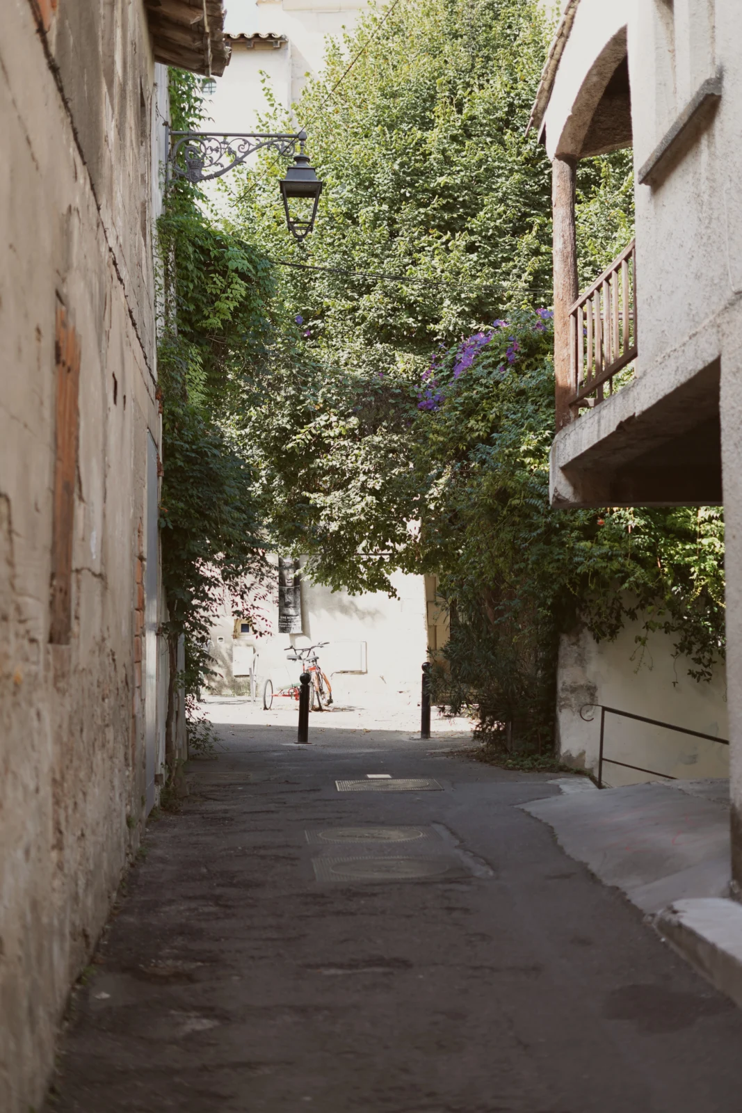 En smal alley med vita stenväggars, grönska, en lykta och en cykel i bakgrunden